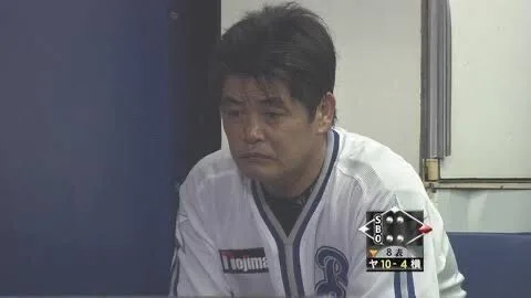 白い野球ユニフォーム姿の男性がベンチで前かがみになっている