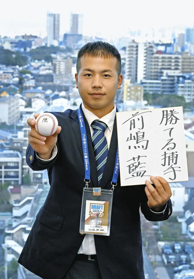 スーツ姿の男性が野球ボールと「前田藍」と書かれた色紙を持っている。