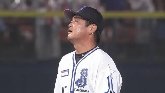 白い野球ユニフォームと黒い帽子を着た選手が、汗をかきながら上を見ている。