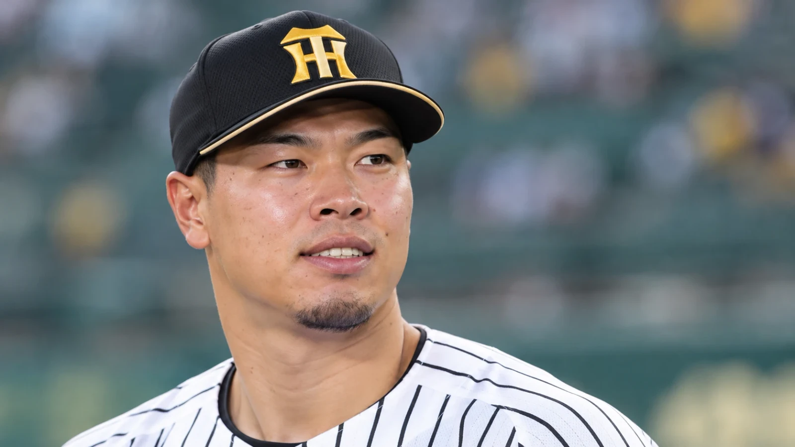 白い縦じまのユニフォームと黒い帽子を着け、横を見つめる野球選手の上半身