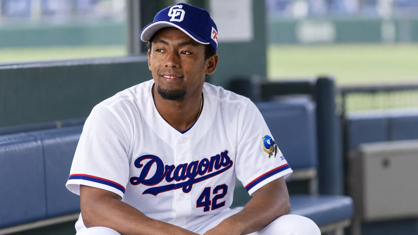 白い野球ユニフォームと青い帽子を着た選手が、ベンチに座っている。