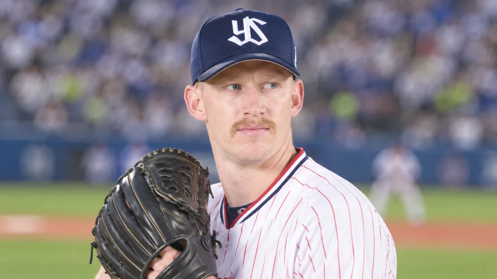 野球帽とユニフォーム姿の投手が、グラブを胸元に構えて球場に立っている