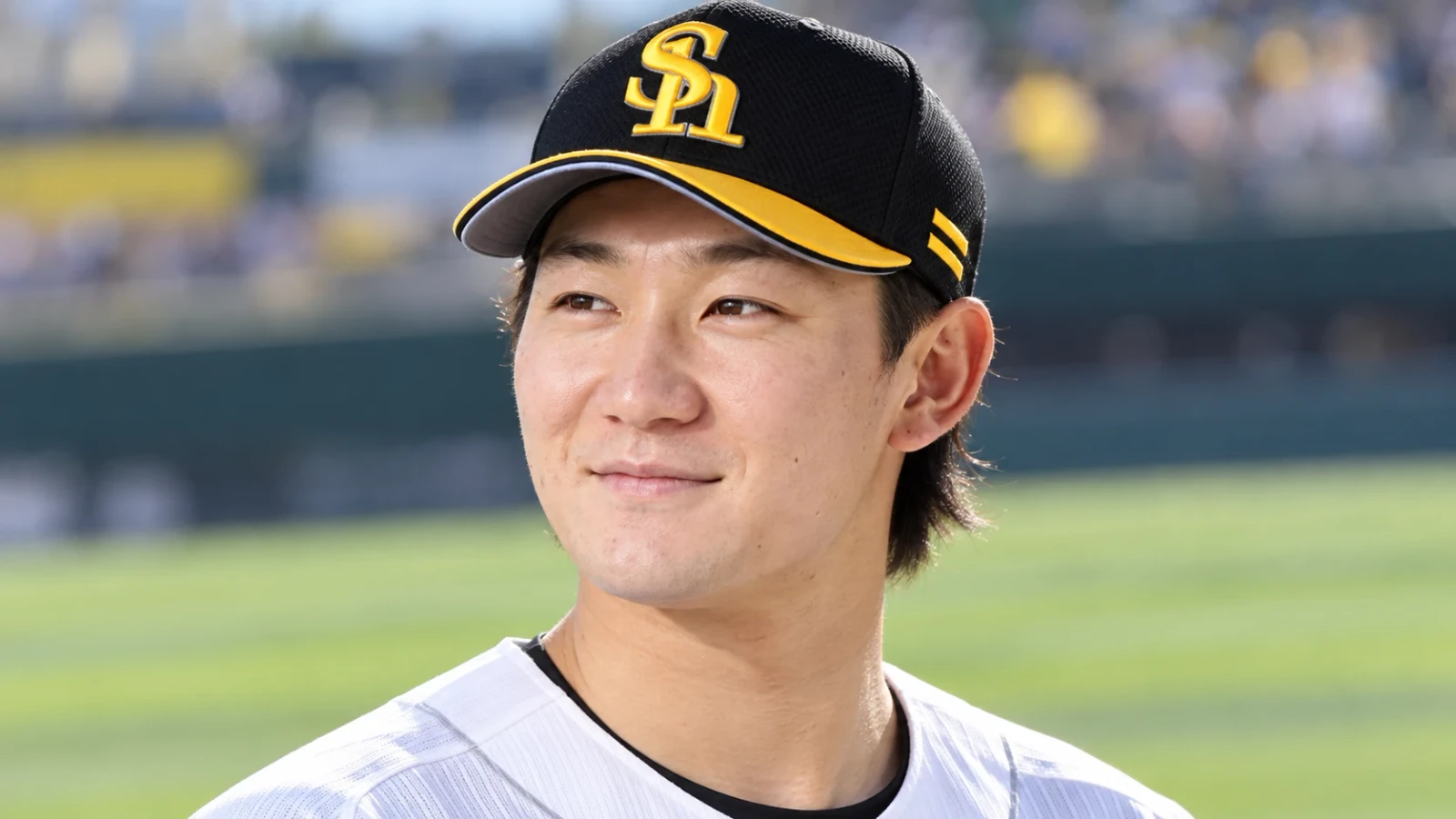 黒と黄色の帽子をかぶった野球選手の顔のアップ。白いユニフォーム姿で、背景に球場の緑のグラウンドがぼけて見える。
