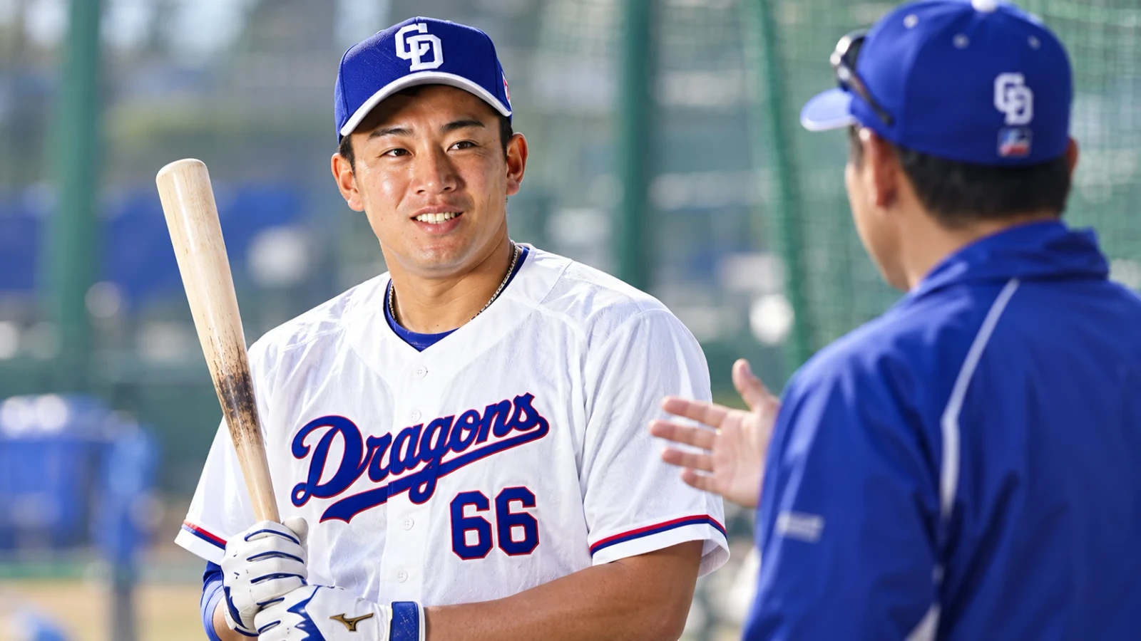 バットを持った野球選手が、練習場で青いウェアの人物と話している