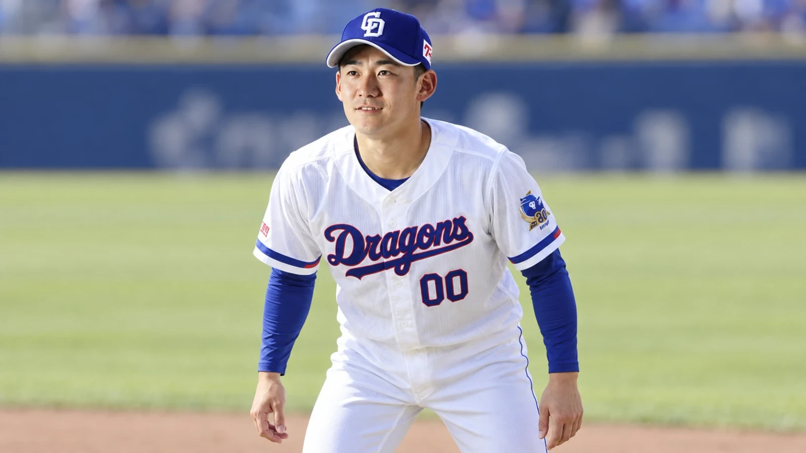 白いユニフォームと青い帽子の野球選手が、グラウンドで腰を落として構えている。